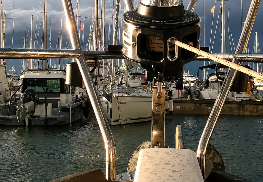 Blick vom Bug eines Segelboots auf eine Rollfockanlage im Yachthafen mit zahlreichen Segelmasten und Booten im Hintergrund.